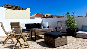 Une terrasse sur le toit, aménagée avec des meubles en osier, une plante en pot et offrant une vue sur les bâtiments en arrière-plan.