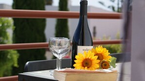 Una botella de vino, una copa y girasoles sobre una mesa con una barandilla al fondo.