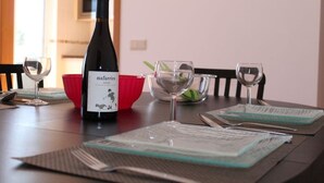Una mesa de comedor con una botella de vino, copas y un tazón rojo.