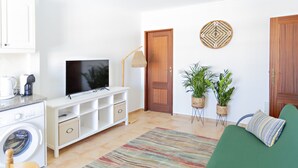 A modern living room with a flat-screen TV, a washing machine, a sofa, and two potted plants. - Cabanas Vintage in Tavira (Tavira)