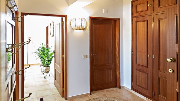 A hallway with a wooden door, a wall-mounted light fixture, and a potted plant. - Cabanas Vintage in Tavira (Tavira)