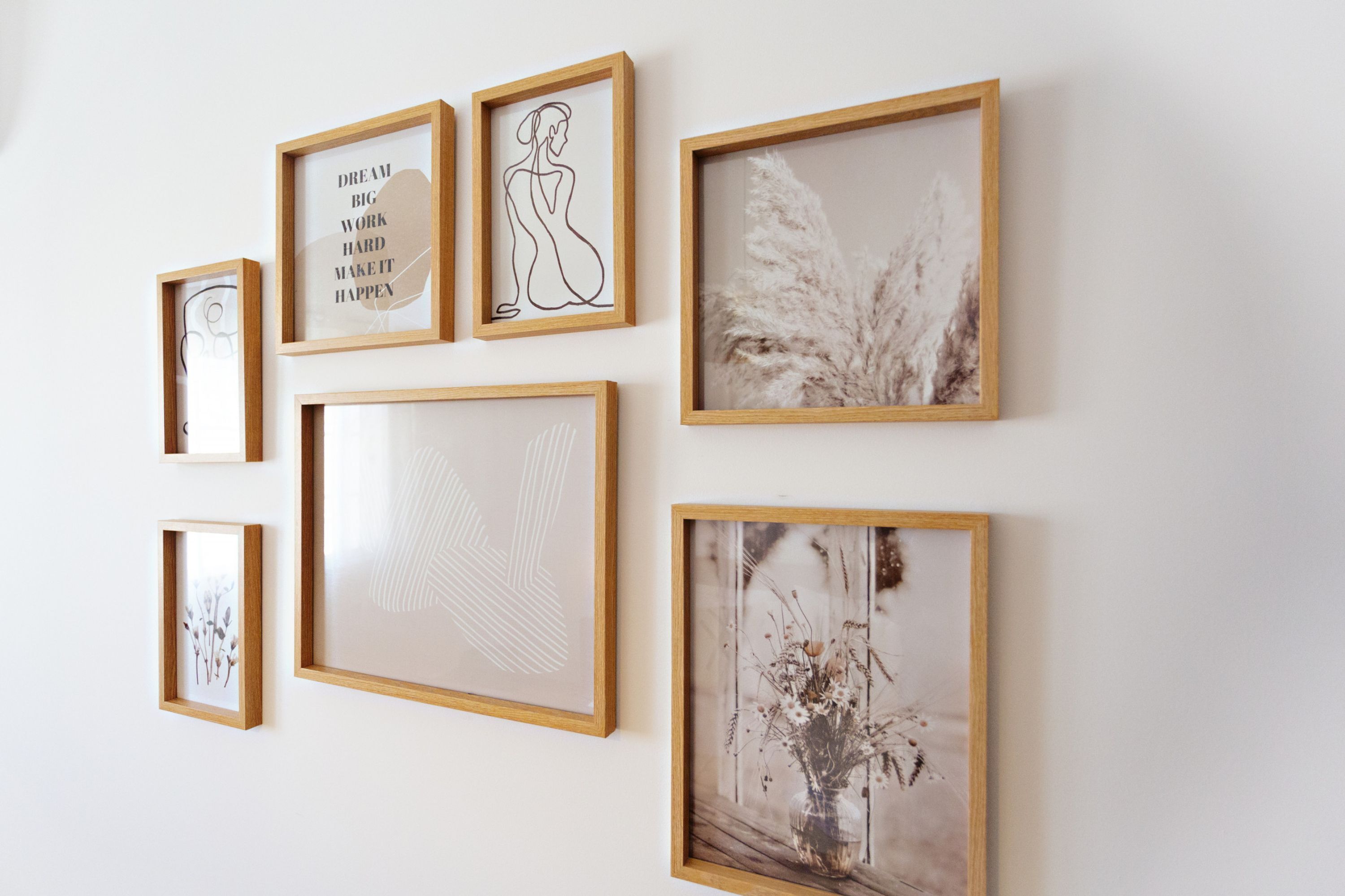 Eine Wand mit verschiedenen gerahmten Kunstwerken, darunter ein Zitat, eine Linienzeichnung und Pflanzenabbildungen.