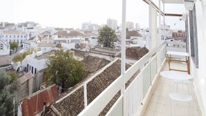 Un balcon donnant sur un paysage urbain, avec des bâtiments et un arbre.