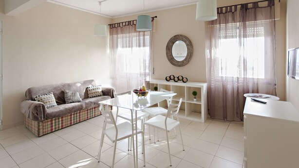 Un salon moderne avec une table à manger en verre, des chaises blanches, un canapé marron agrémenté de coussins à motifs et un meuble blanc.