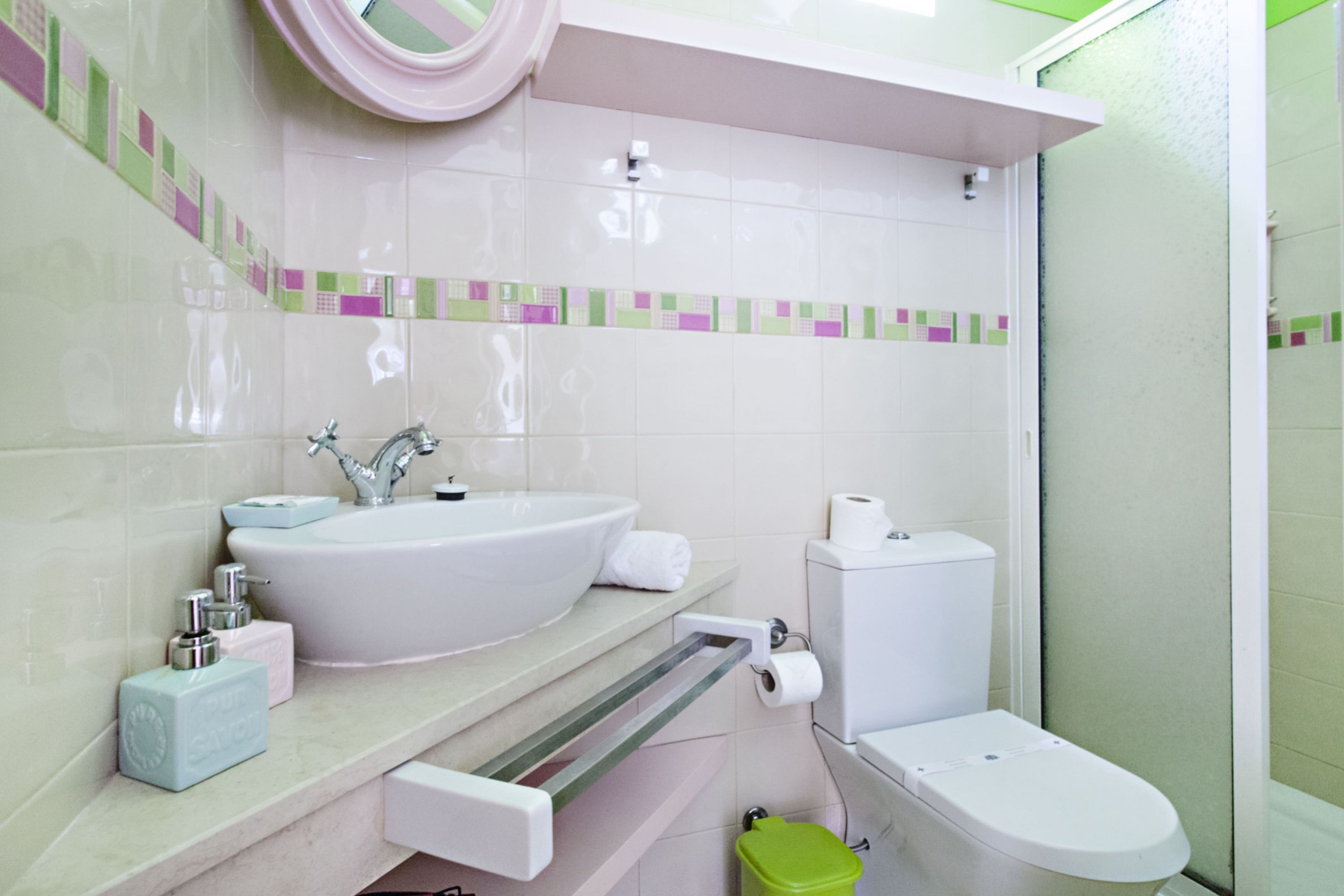 A bathroom with a white sink, toilet, and green trash bin.