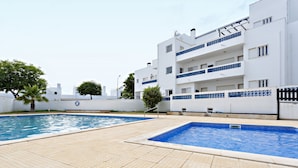 A swimming pool area with tiled flooring and a white building with balconies. - Lavender in Tavira With 2 Bedrooms and 2 Bathrooms (Tavira)