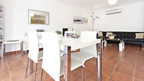 A modern living room with a dining area, featuring a white dining table, chairs, a black leather sofa, and a coffee table. - Lavender in Tavira With 2 Bedrooms and 2 Bathrooms (Tavira)