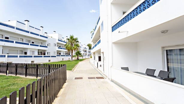 A corridor with a wooden fence, a tiled walkway, and white buildings with blue accents. - Lavender in Tavira With 2 Bedrooms and 2 Bathrooms (Tavira)