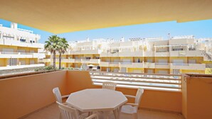 Ein Balkon mit weißem Tisch und Stühlen, der auf ein Wohngebiet mit gelben Gebäuden und einer Palme blickt.