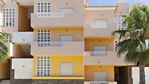 Ein mehrstöckiges Wohngebäude mit Balkonen, einer gelben Fassade und einer Palme im Vordergrund.