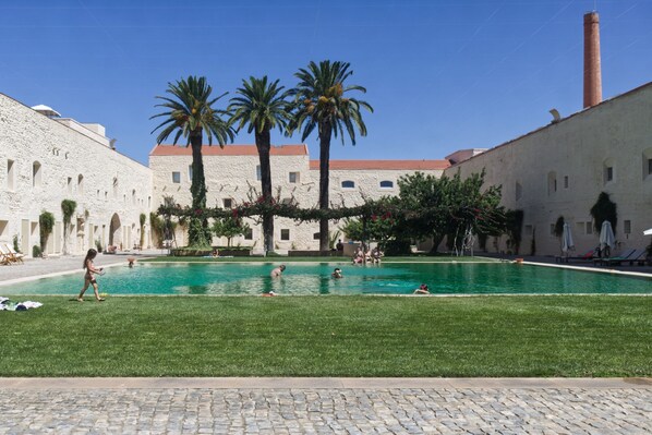 A courtyard with a swimming pool, palm trees, and stone buildings. - CV AI- Convento das Bernardas (Tavira)