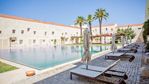 A poolside area with lounge chairs and umbrellas, a clear pool, and a building with a tiled roof in the background. - CV AI- Convento das Bernardas (Tavira)