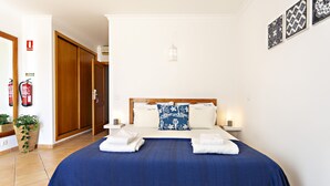 A hotel room with a large bed, wooden wardrobe, and a small bedside table with a lamp. - QV 119 - Le Bleu Studio - Quinta Velha (Tavira)