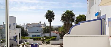 A rooftop terrace with a pool, palm trees, and a view of the cityscape.