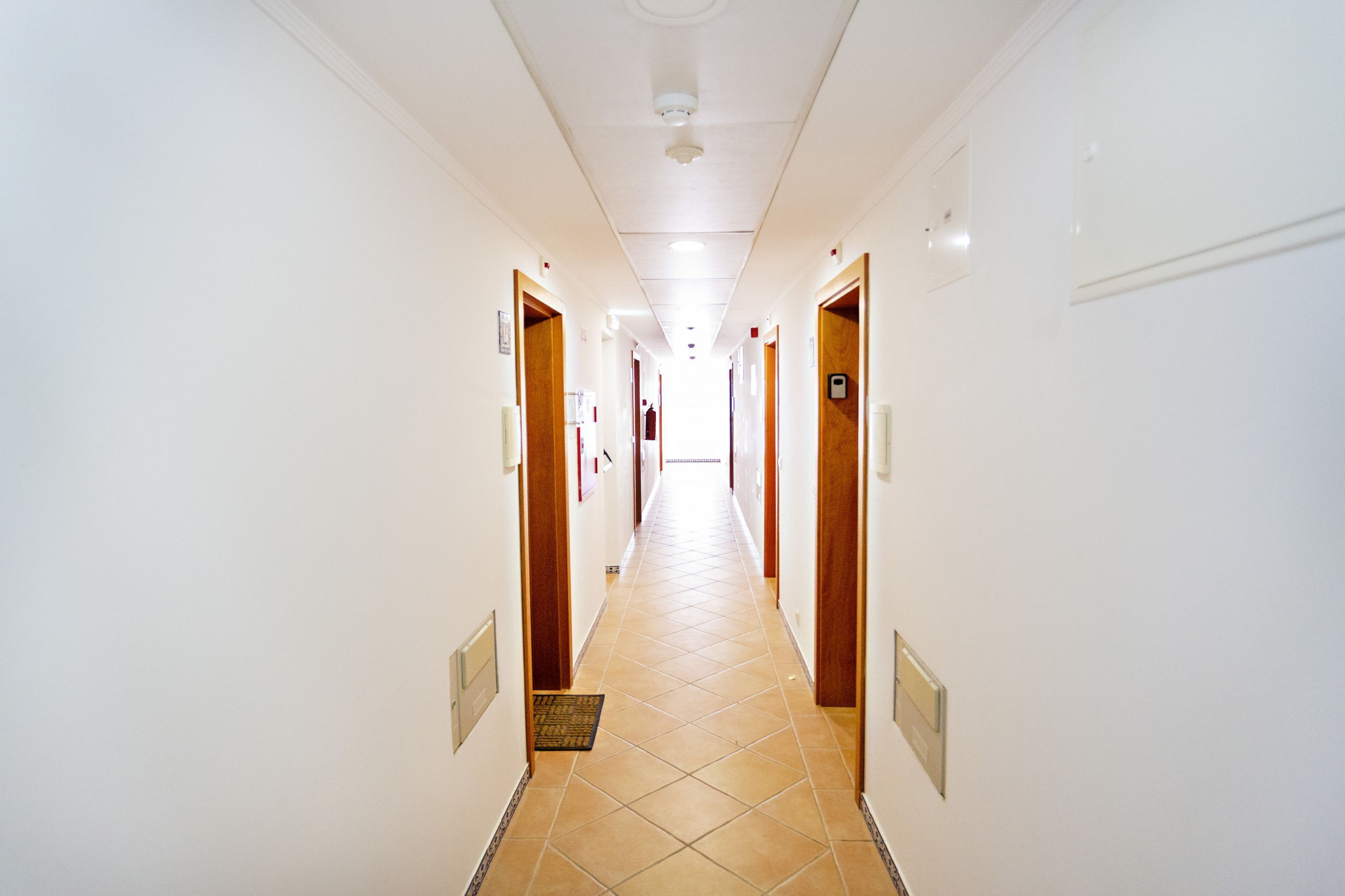 A long, narrow hotel corridor with white walls and a tiled floor.