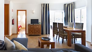 A living room with a sofa, a dining table with chairs, a TV, and a fireplace. - QV 10 - Terrace of Peace Apartment - Quinta Velha (Tavira)