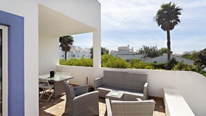 A balcony with wicker furniture, a table, and chairs. - QV 10 - Terrace of Peace Apartment - Quinta Velha (Tavira)
