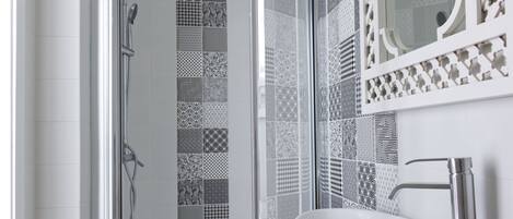 A bathroom with a glass shower enclosure, a white sink, and a patterned tile backsplash.