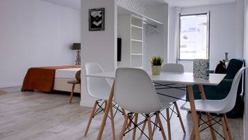 A modern, well-lit room with a dining table, white chairs, and a sofa.
