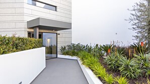 A modern building with a flat facade, a glass entrance, and a landscaped garden with various plants. - My Ocean View in Tavira (Tavira)
