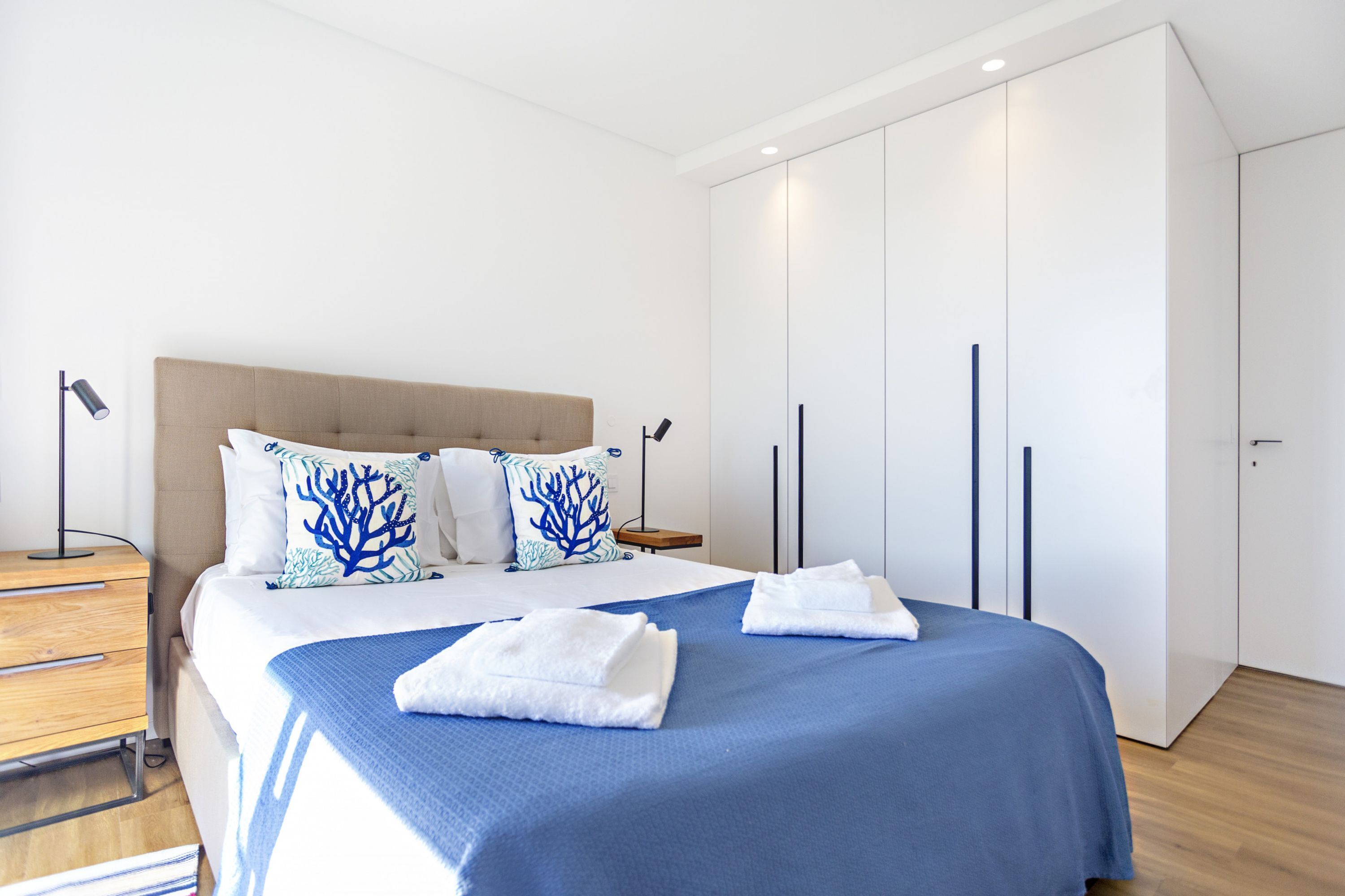 Una habitación de hotel moderna con una cama grande, una mesita de noche de madera, un armario y un escritorio.