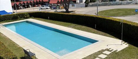 A rectangular swimming pool with a clear blue water, surrounded by a well-maintained lawn and a hedge.