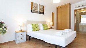 A hotel room with a bed, bedside tables, a nightstand, a potted plant, and artwork on the wall. - Cam lia in Tavira With 2 Bedrooms and 2 Bathrooms (Tavira)