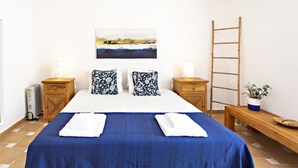 A neatly arranged hotel room with a large bed, two nightstands, a wooden ladder, a bench, and a potted plant.