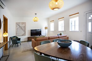 A modern living room with a wooden dining table, a sofa, and a television. - Pink House in Faro With 3 Bedrooms and 3 Bathrooms (Faro)