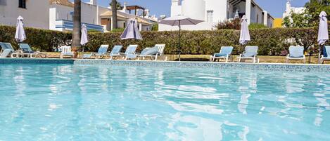 Una piscina con lettini e ombrelloni, circondata da edifici bianchi e palme.