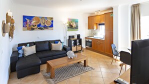 A living room with a sofa, coffee table, and artwork on the wall. - QV 21 - Straw Hat Apartment - Quinta Velha (Tavira)