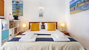 A hotel room with a large bed, two bedside tables, a shelf with storage boxes, and two paintings on the walls. - QV 20 - Saltwater Apartment - Quinta Velha (Tavira)