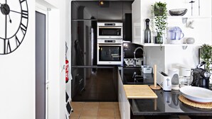 A modern kitchen with black appliances, a wooden cutting board, and a coffee maker. - QV 210 - Black White Apartment - Quinta Velha (Tavira)
