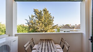 Een balkon met een houten tafel en comfortabele stoelen, met uitzicht op bomen en gebouwen.