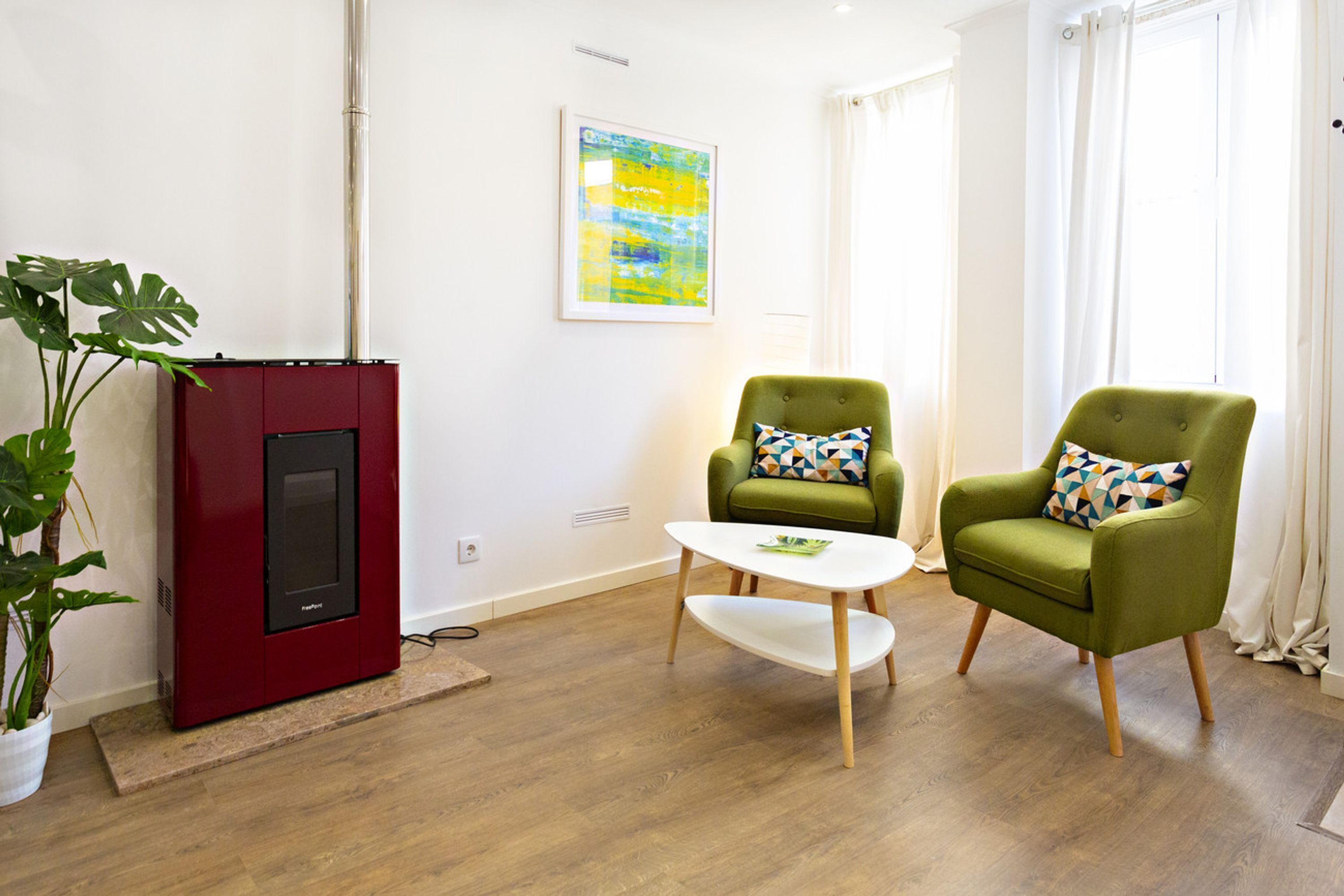 Een moderne woonkamer met een rode open haard, twee groene fauteuils, een witte salontafel en een groot raam met gordijnen.