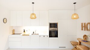 Une cuisine moderne avec des meubles blancs, un évier en acier inoxydable et deux luminaires suspendus.