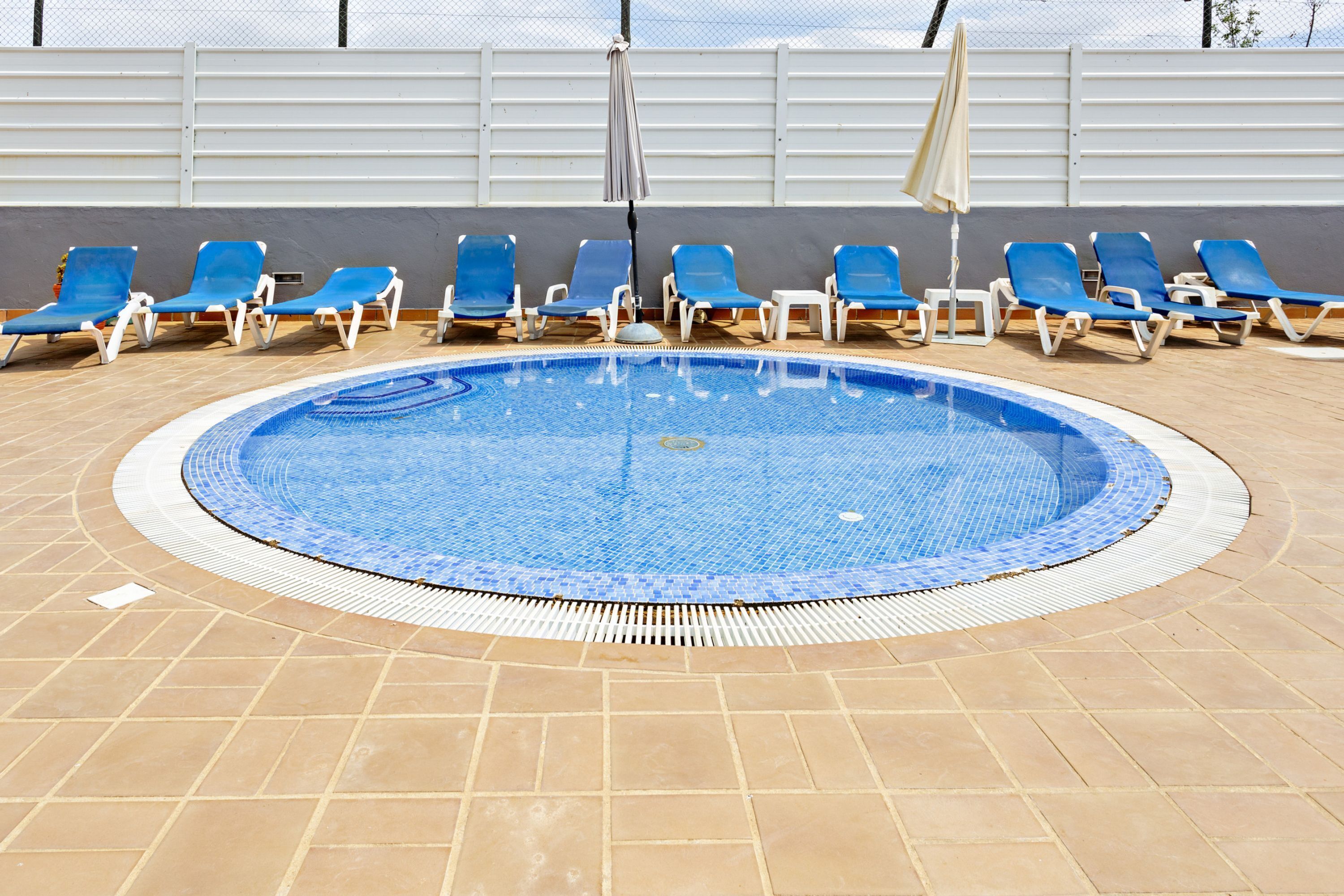 A swimming pool with blue tiles, surrounded by blue and white lounge chairs, and a tiled deck.