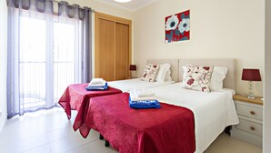 A hotel room with two beds, a large window with curtains, a painting on the wall, and a bedside table with a lamp. - CB Miranda - Cabanas Beach (Tavira)