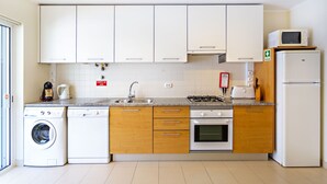 A modern kitchen with white cabinets, a built-in oven, a microwave, and a washing machine. - CB Miranda - Cabanas Beach (Tavira)