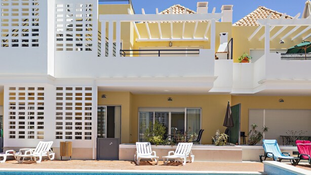 A pool area with white lounge chairs, a covered seating area, and a clear blue pool. - CB Miranda - Cabanas Beach (Tavira)