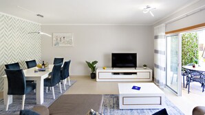 A modern living room with a dining area, a flat-screen TV, and a sliding glass door to the outdoors.