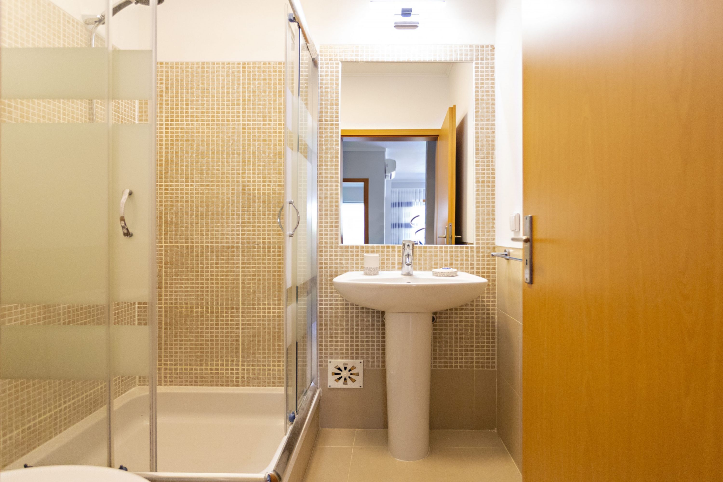 A bathroom with a glass-enclosed shower, a pedestal sink, and tiled walls.