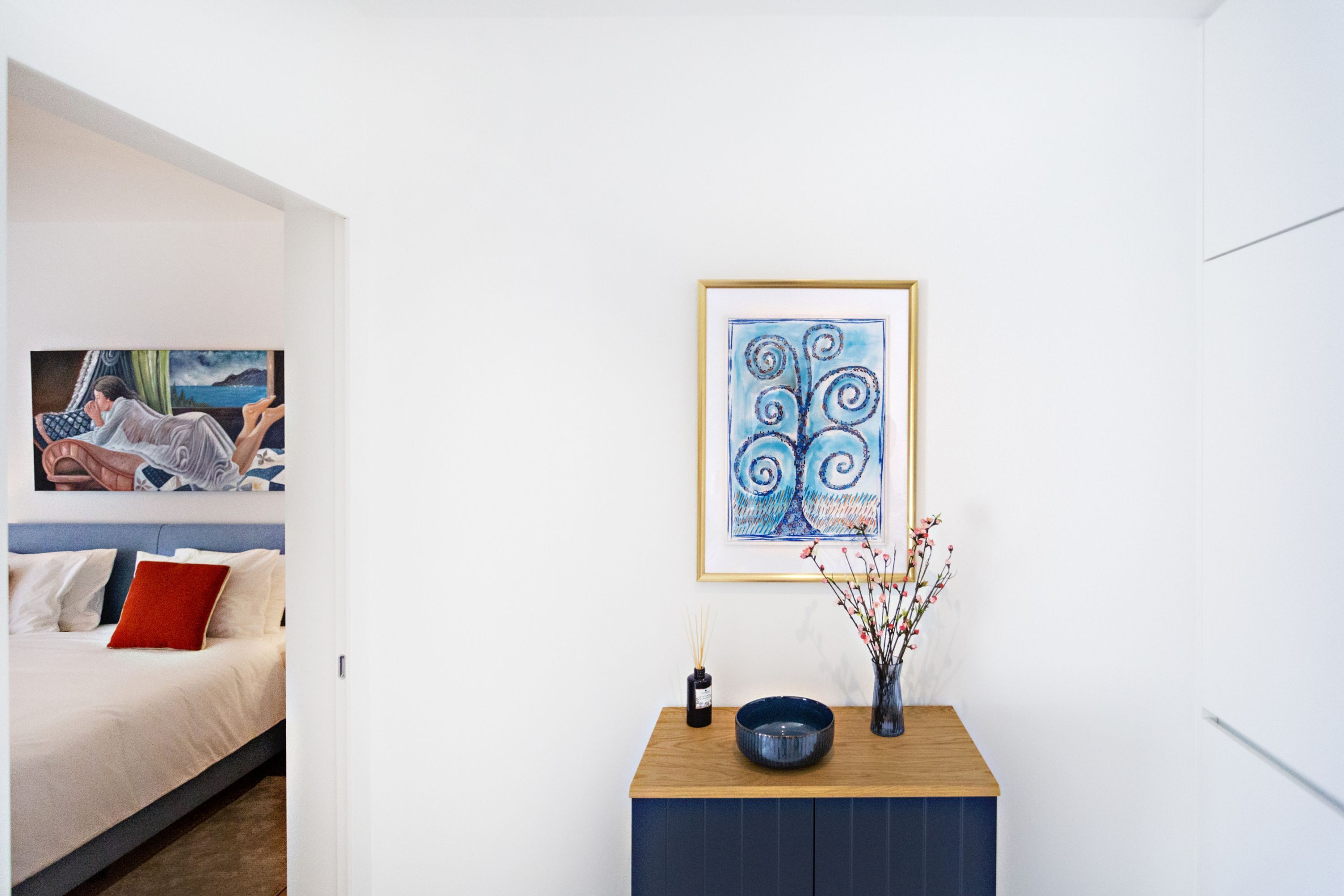 Un dormitorio moderno con cama, mesita de noche con un florero y un cuadro abstracto enmarcado en la pared.