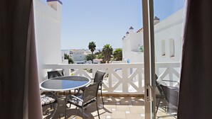 A balcony with a table and chairs, a white railing, and a view of buildings and palm trees.