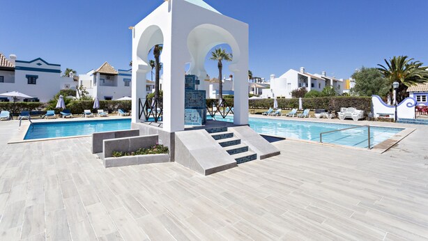 A swimming pool area with a modern gazebo structure, lounge chairs, and a clear blue sky.