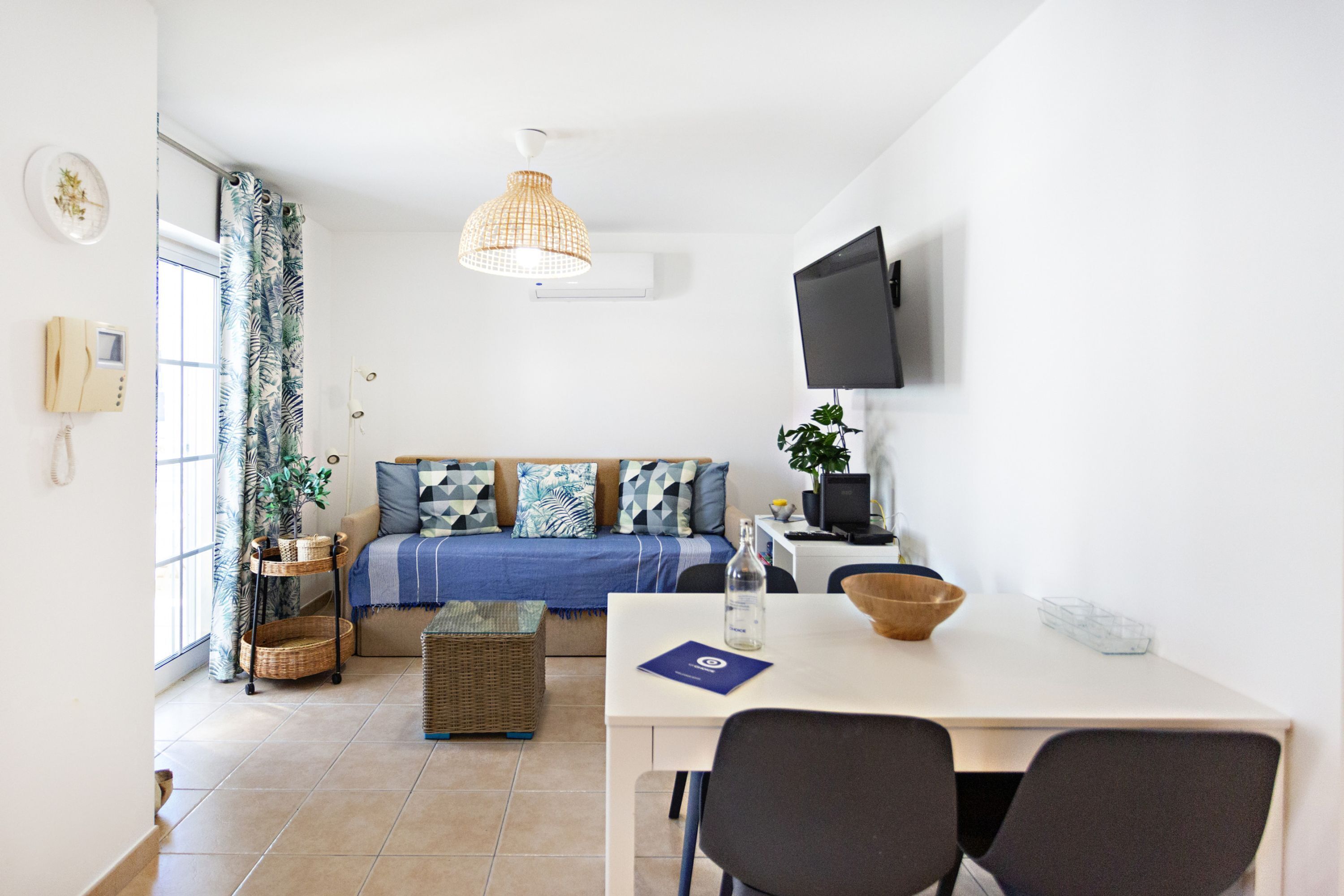 Un salón moderno y bien iluminado con un sofá, una mesa de comedor y un televisor montado en la pared.