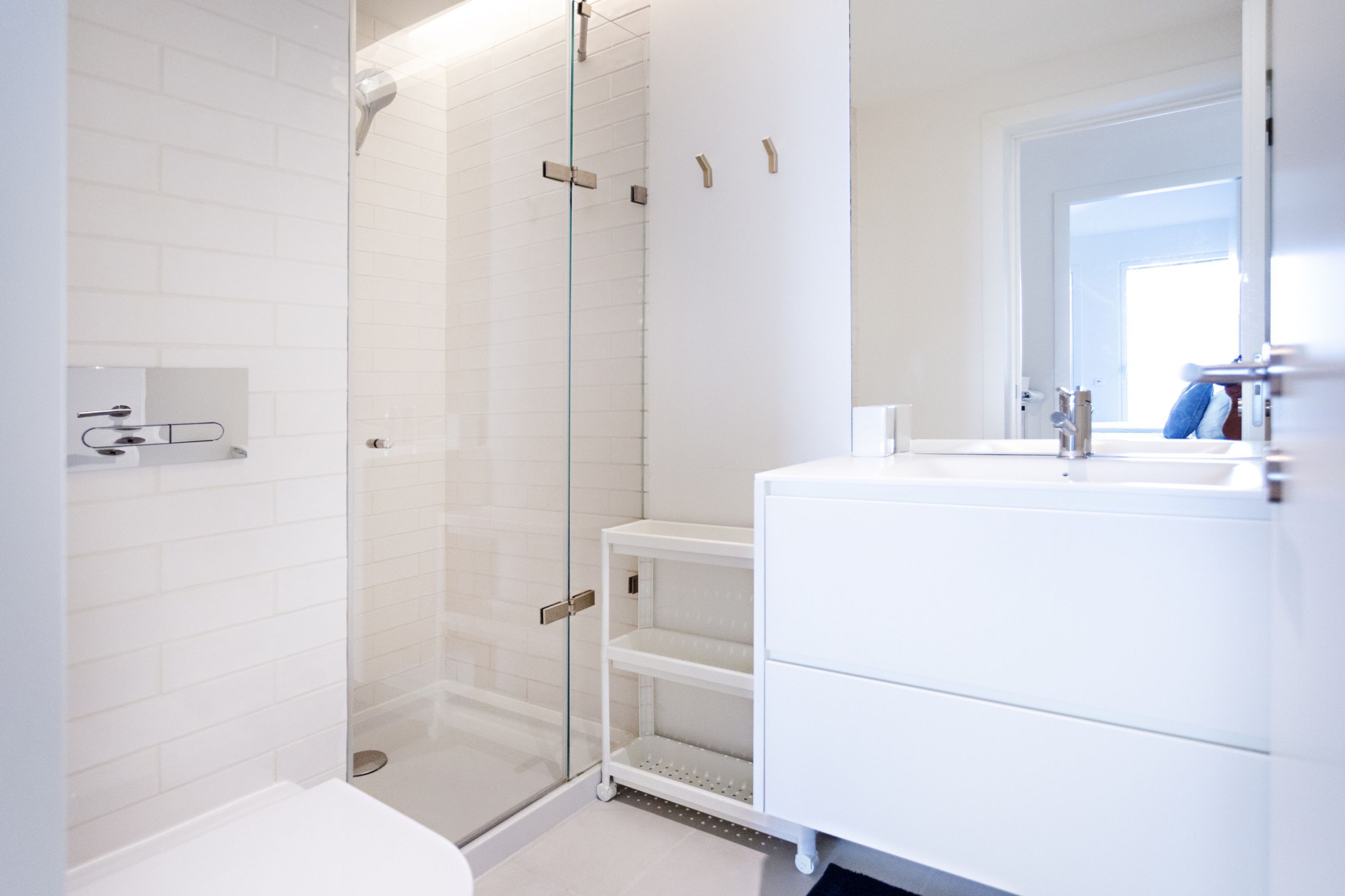 A modern bathroom with a glass shower enclosure, white tiled walls, and a white vanity with a mirror.