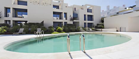 A modern building with a pool, outdoor seating, and a clear sky.