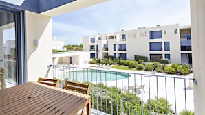 Un balcon avec une table et des chaises en bois, donnant sur une piscine et un immeuble doté de nombreux balcons.