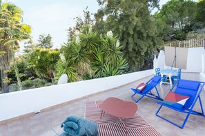Relax on the rooftop terrace with a view of lush greenery and trees, surrounded by comfortable lounge chairs and a dining table.